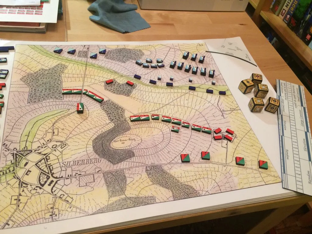 Mesa con un mapa topográfico antiguo, reglas de medición metálicas y pequeños bloques rectangulares de colores que representan unidades militares
