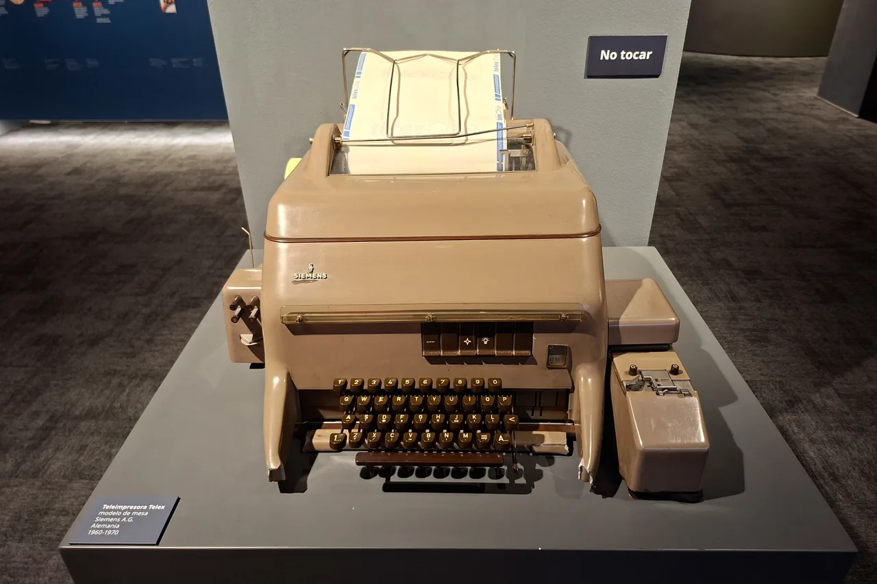 Una teleimpresora de télex Teleimpresora de télex Siemens color café con teclado y rollo de papel, exhibida sobre un pedestal gris