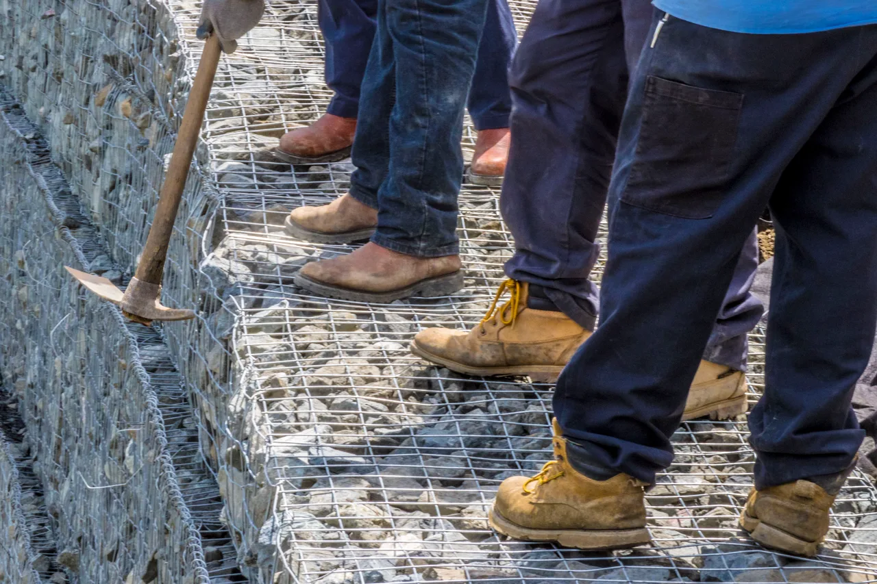 Trabajos de reconstrucción tras María Botas de trabajo sobre gaviones de piedra durante una reconstrucción